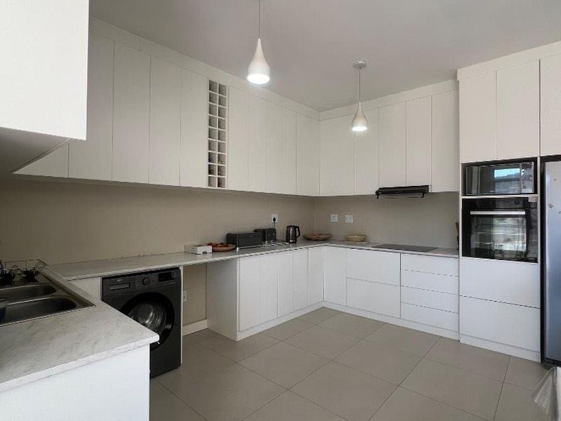 Modern kitchen featuring white cabinetry, stone countertops, integrated appliances, and tiled flooring, offering a clean and functional workspace.
