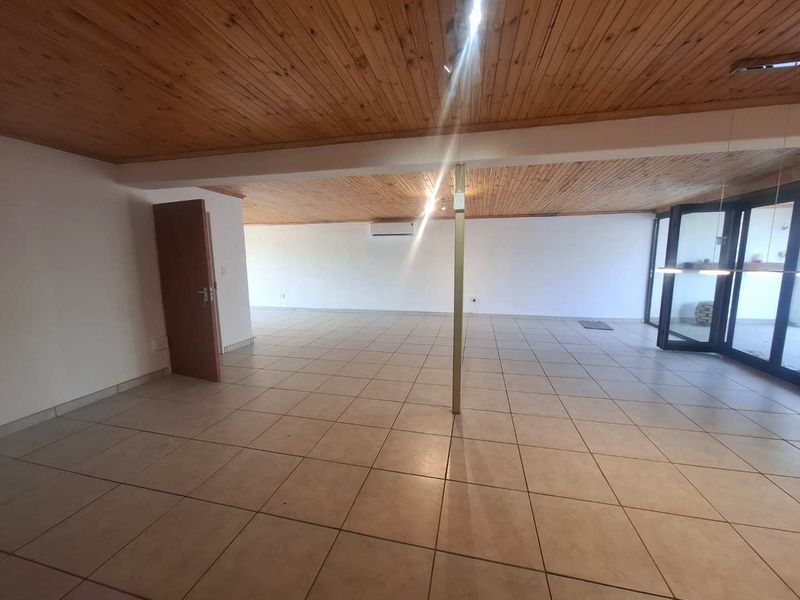 Spacious open-plan living area featuring ceramic floor tiles, a timber tongue and groove ceiling, and bi-fold doors leading to an outdoor space.