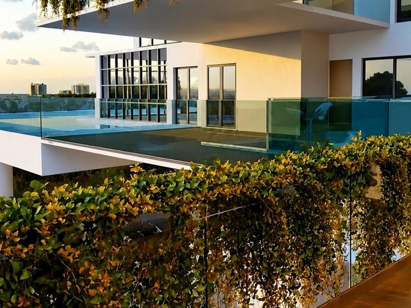 Modern apartment balcony featuring glass balustrades and integrated vertical greenery, offering a sleek architectural design with expansive outdoor living space.