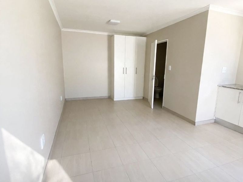 A bright, empty bedroom featuring neutral tiled flooring, a built-in wardrobe, and direct access to an en-suite bathroom.