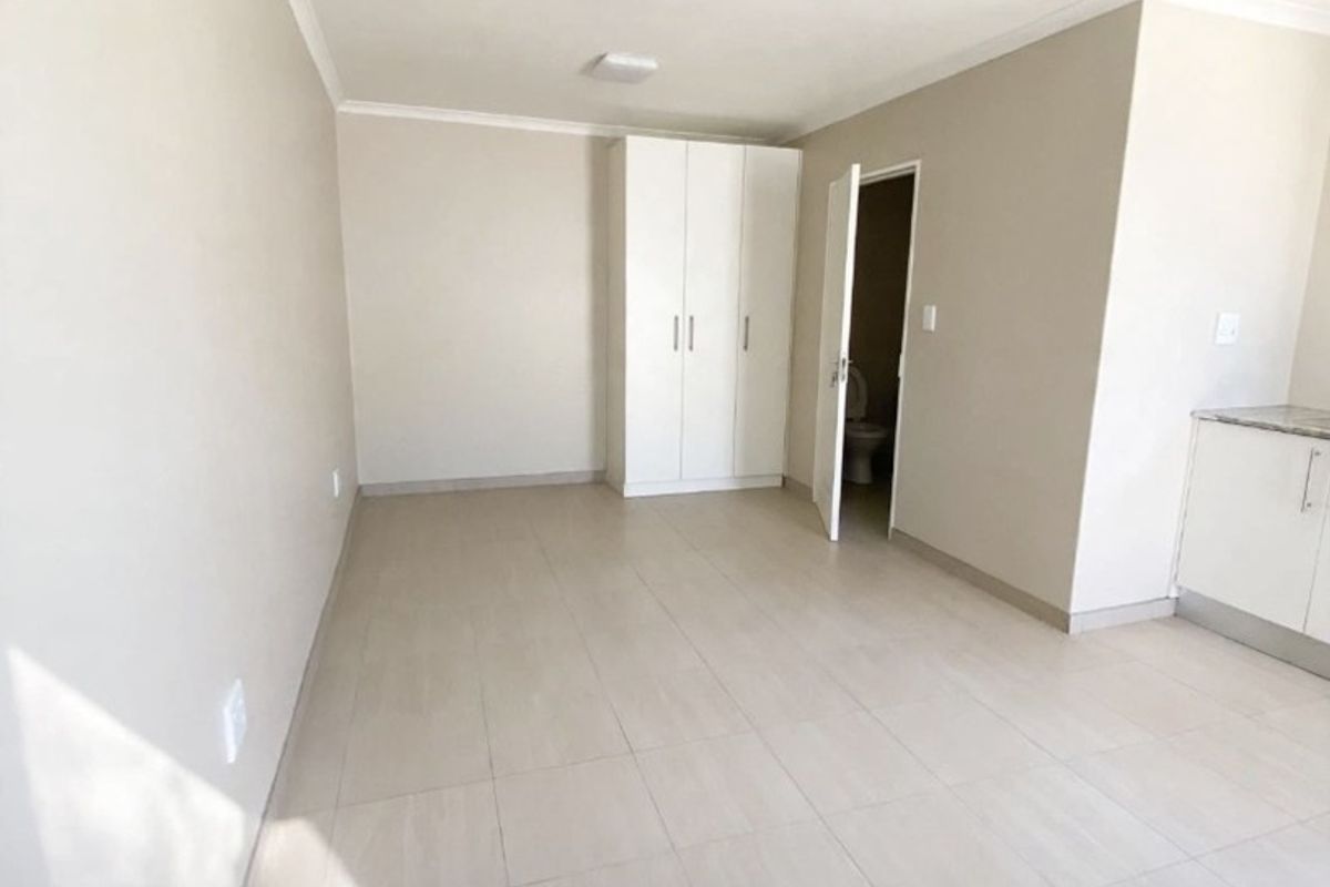 A bright, empty bedroom featuring neutral tiled flooring, a built-in wardrobe, and direct access to an en-suite bathroom.