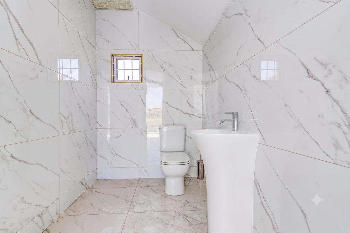 A modern, clean bathroom featuring marble-effect wall tiles, a pedestal basin, and a toilet, finished with neutral floor tiling.