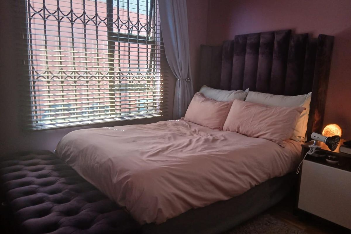 A cozy bedroom featuring a large window with fitted security bars and blinds, providing natural light to the space.