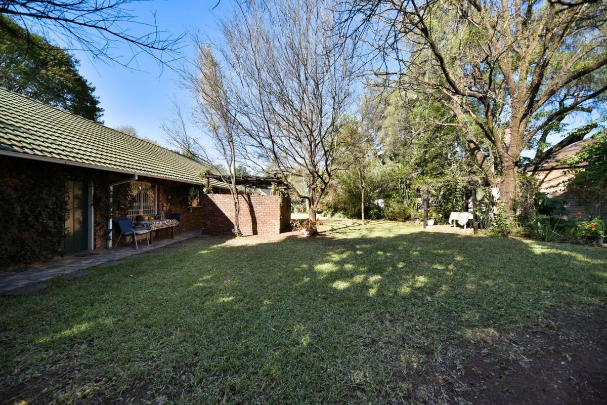 A spacious rear garden featuring a paved patio area, established trees, and a brick-walled section adjacent to the main house structure.