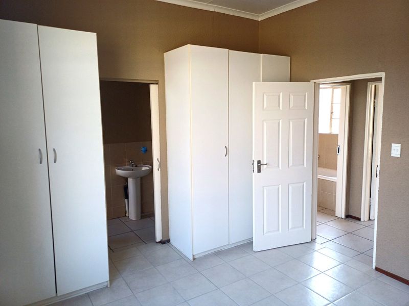 A spacious bedroom featuring built-in cupboards, tiled flooring, and direct access to an en-suite bathroom with a pedestal basin and bathtub.