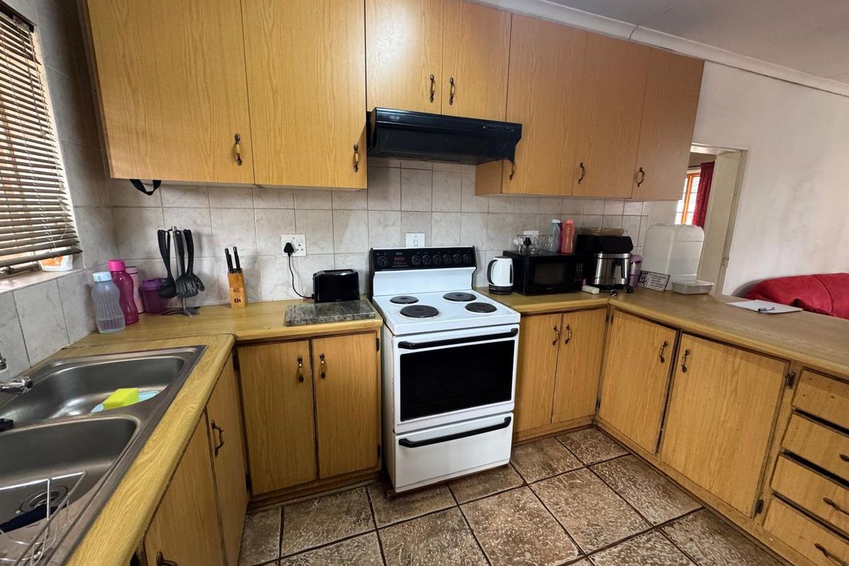 Functional kitchen featuring wood-look cabinetry, tiled backsplash, double basin sink, and a freestanding electric stove with an extractor fan.