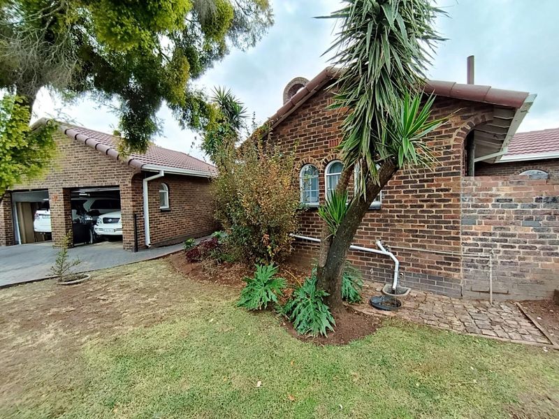 Front view of a brick house featuring a double garage, arched windows, and a landscaped garden area.