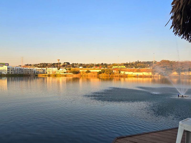 A scenic view overlooking a tranquil lake with a central water fountain, captured from a wooden deck area.