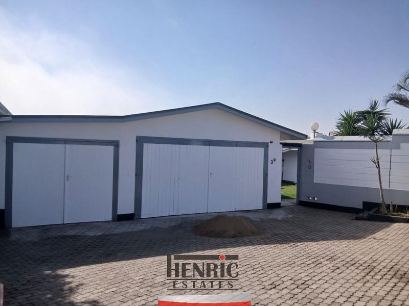 Front exterior view of the property featuring a double garage with white doors, a paved driveway, and a secure boundary wall.