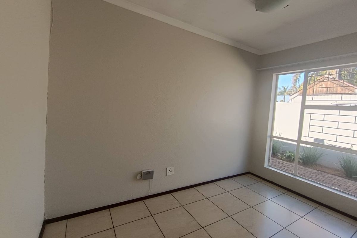 A bright, empty bedroom featuring neutral tiled flooring, a large window providing natural light, and standard electrical fixtures.