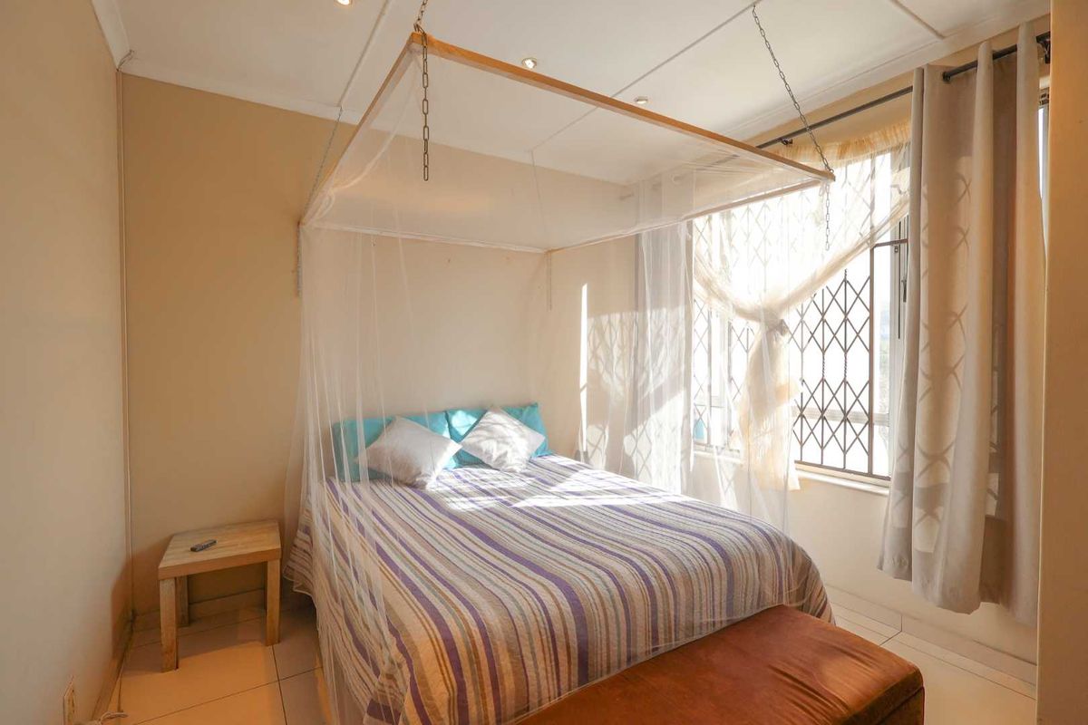 A cozy bedroom featuring tiled flooring, a window with security bars, and recessed ceiling lighting.