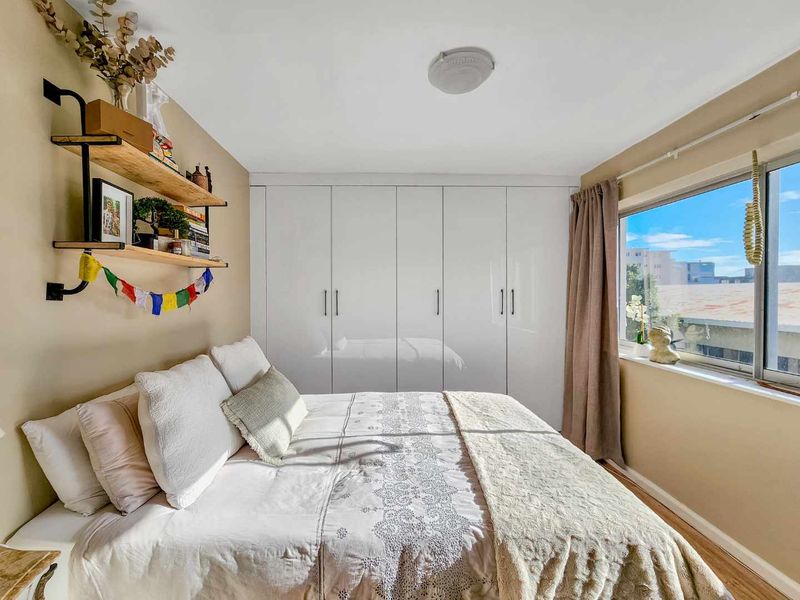 A well-maintained bedroom featuring built-in white cupboards, laminate flooring, and a window providing natural light.