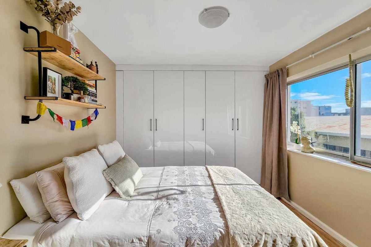 A well-maintained bedroom featuring built-in white cupboards, laminate flooring, and a window providing natural light.