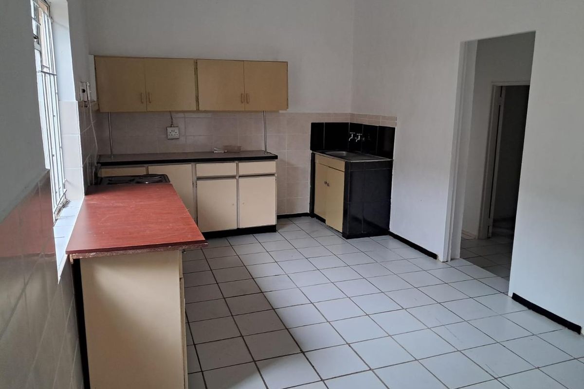 A functional, empty kitchen featuring tiled flooring, built-in cabinetry, and a stainless steel sink, offering a blank canvas for modern renovation.