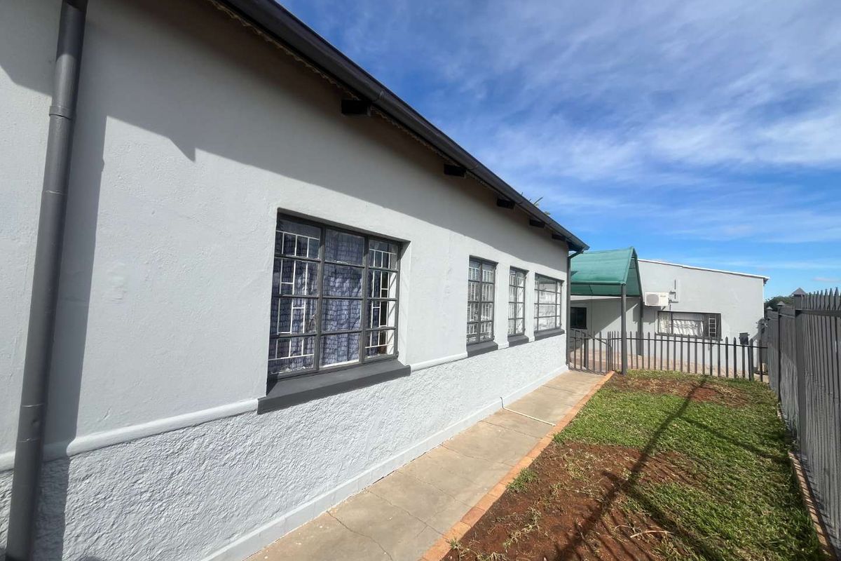 A view of the side exterior of the house featuring a paved walkway, metal security window bars, and a small grassed area.