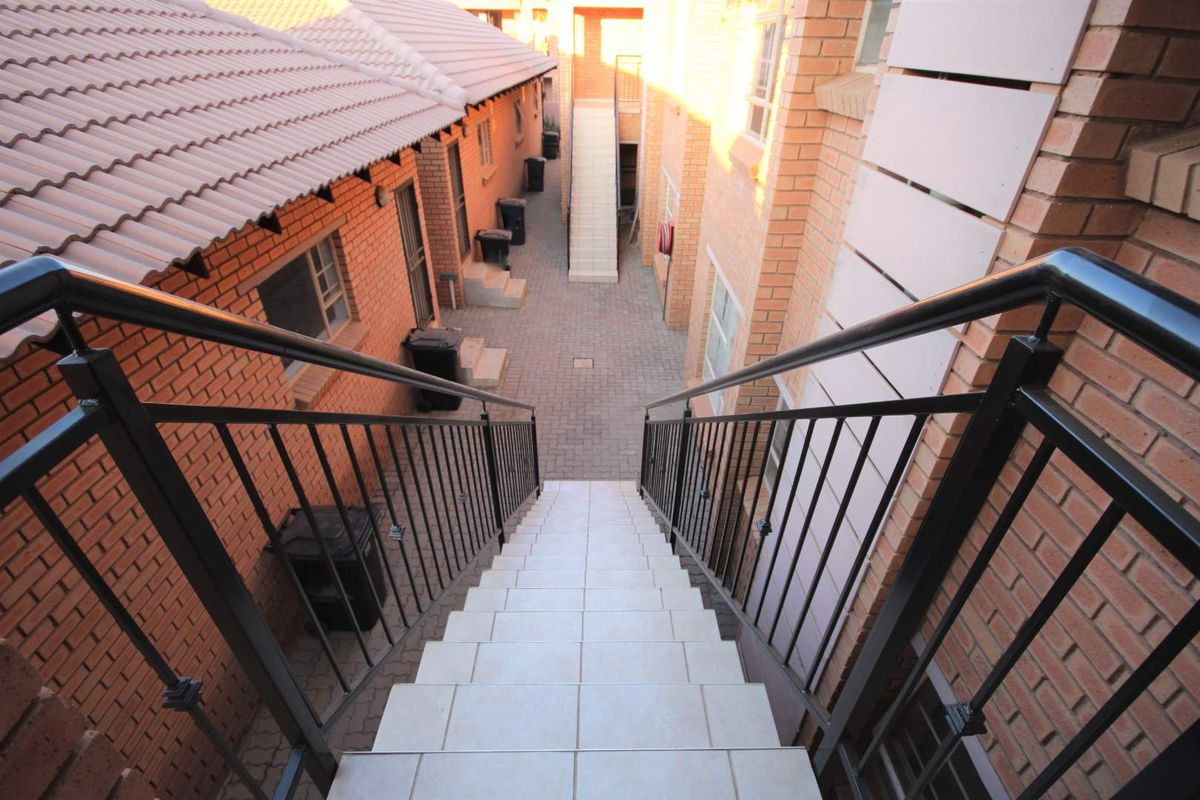 An elevated view of a paved apartment complex courtyard featuring brick buildings, tiled staircases, and metal safety railings.