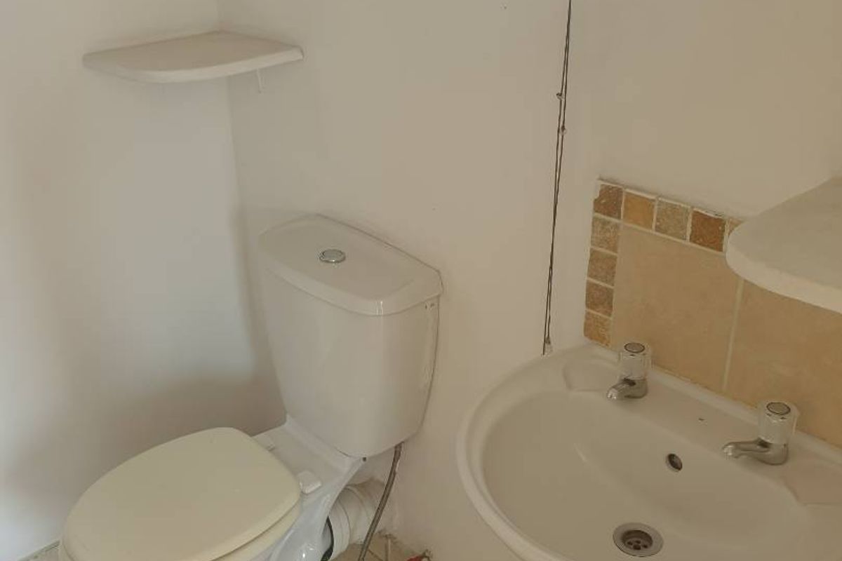 A compact bathroom featuring a pedestal sink, toilet, and tiled flooring, requiring cosmetic updates to modernize the space.
