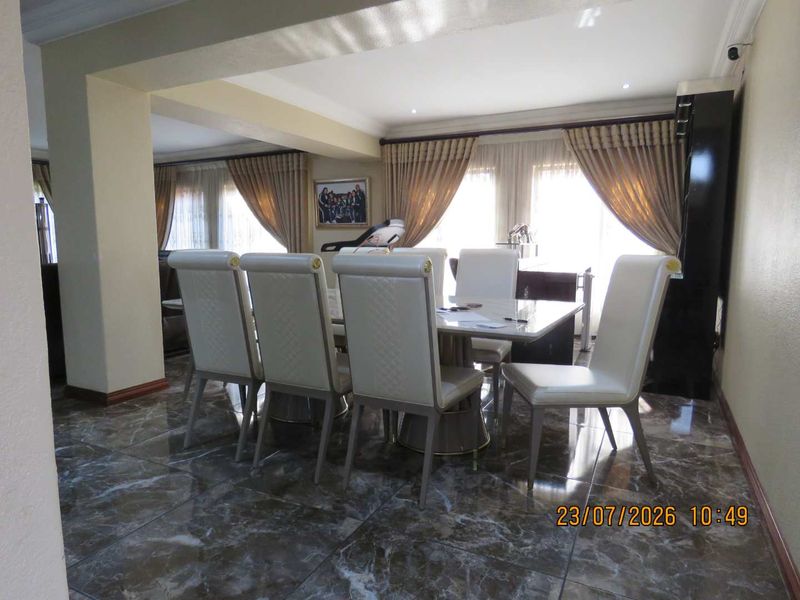 A formal dining area featuring polished marble-look floor tiles, coved ceiling detailing, and recessed lighting, creating a bright and open space.
