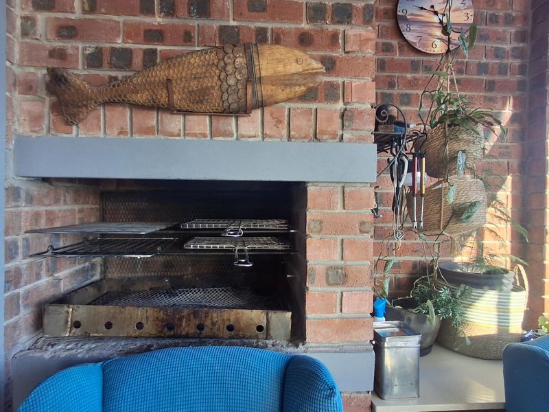 A covered patio area featuring a traditional built-in brick braai with a metal firebox, ideal for outdoor entertaining and cooking.