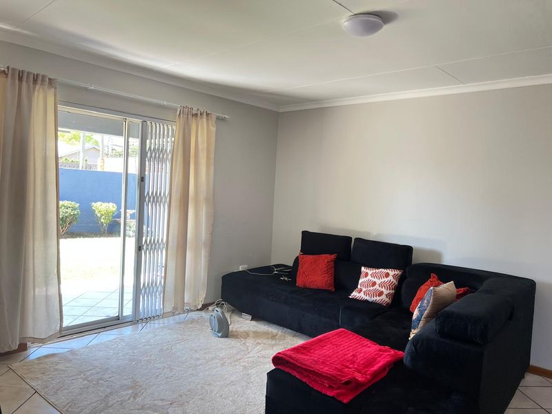A bright living room featuring tiled flooring and a sliding glass door with a security gate, providing direct access to the outdoor patio area.
