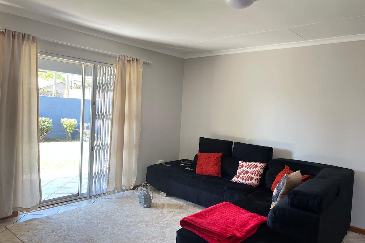 A bright living room featuring tiled flooring and a sliding glass door with a security gate, providing direct access to the outdoor patio area.