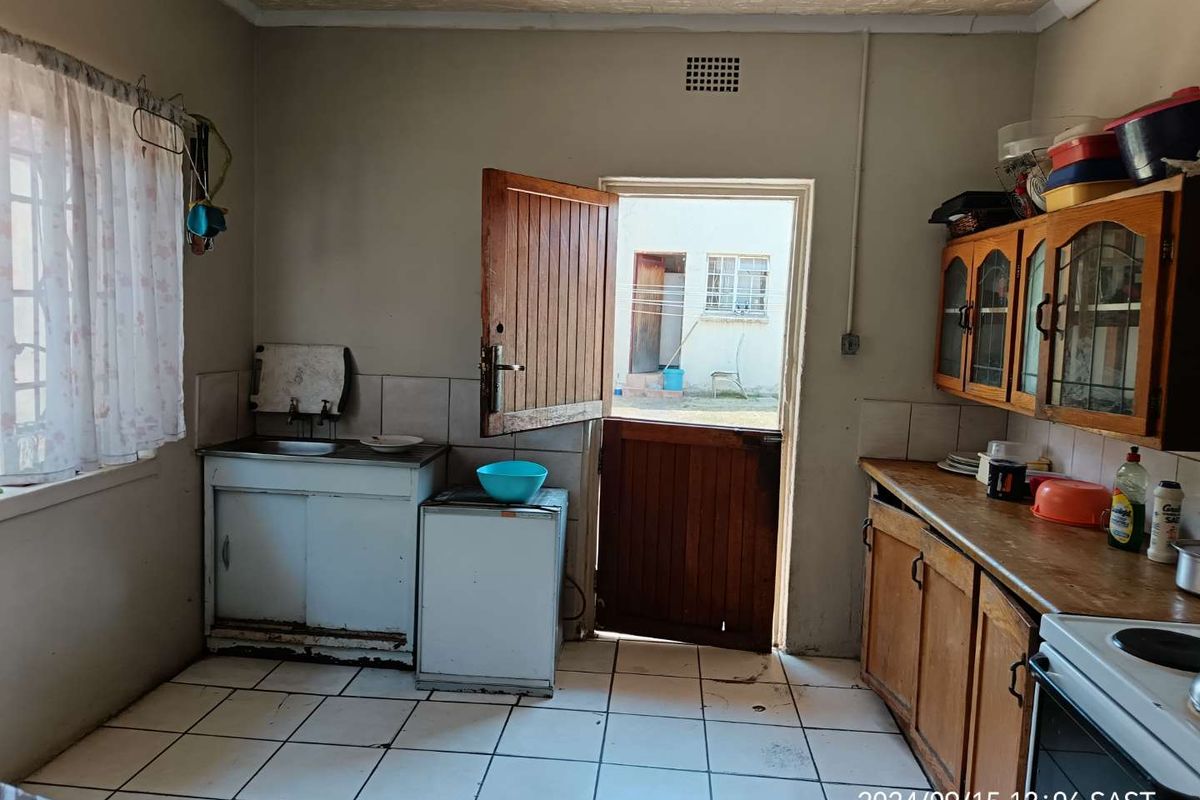 A dated kitchen featuring wooden cabinetry, tiled flooring, and a stable-style door leading to the exterior.