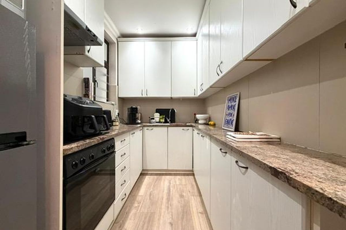 A functional galley-style kitchen featuring white cabinetry, laminate countertops, integrated oven, and wood-look flooring, offering efficient workspace and storage.