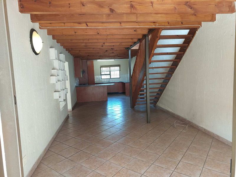 Open plan living and kitchen area featuring exposed timber ceiling beams, a wooden staircase, and tiled flooring throughout.