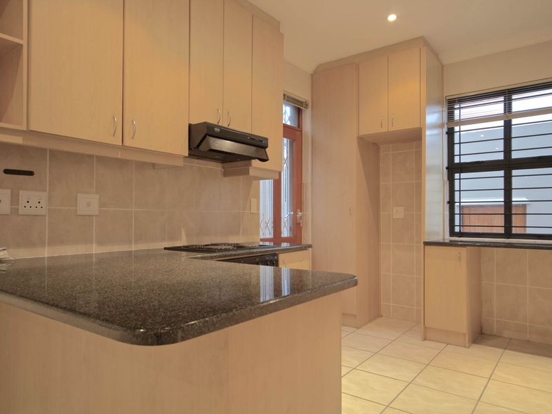 A clean, functional kitchen featuring light wood cabinetry, granite countertops, a built-in hob with extractor fan, and tiled flooring throughout.