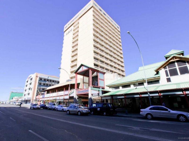 Street-level view of a multi-story commercial building featuring retail storefronts and a prominent covered entrance in a busy urban setting.