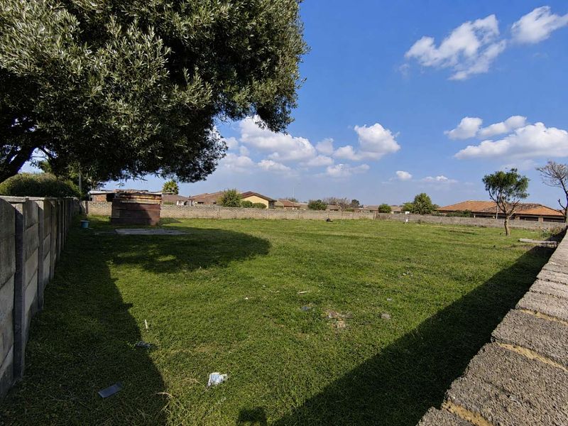 A spacious, level residential plot featuring a grass lawn, perimeter boundary walls, and a mature tree, offering a clear space for future development.