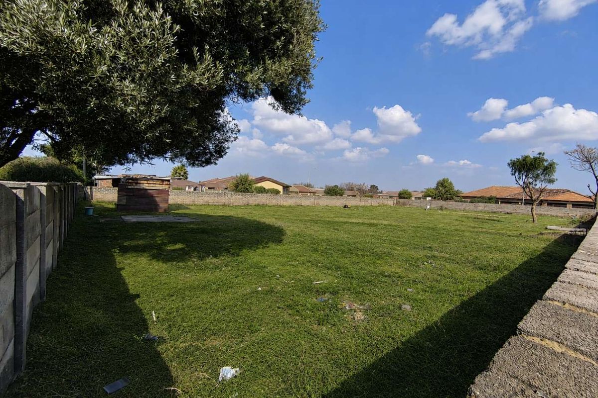 A spacious, level residential plot featuring a grass lawn, perimeter boundary walls, and a mature tree, offering a clear space for future development.