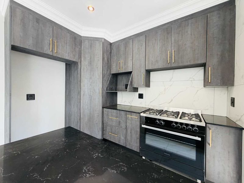 Modern kitchen featuring grey wood-look cabinetry, black marble-effect countertops, white marble splashback, and a high-quality freestanding gas stove.