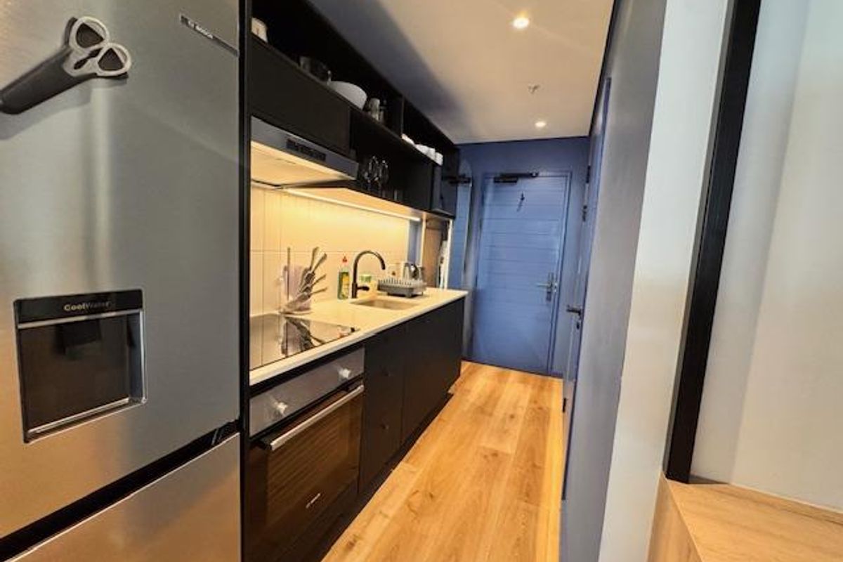 Modern galley-style kitchen featuring sleek dark cabinetry, integrated oven, hob, extractor fan, and light wood-look flooring.