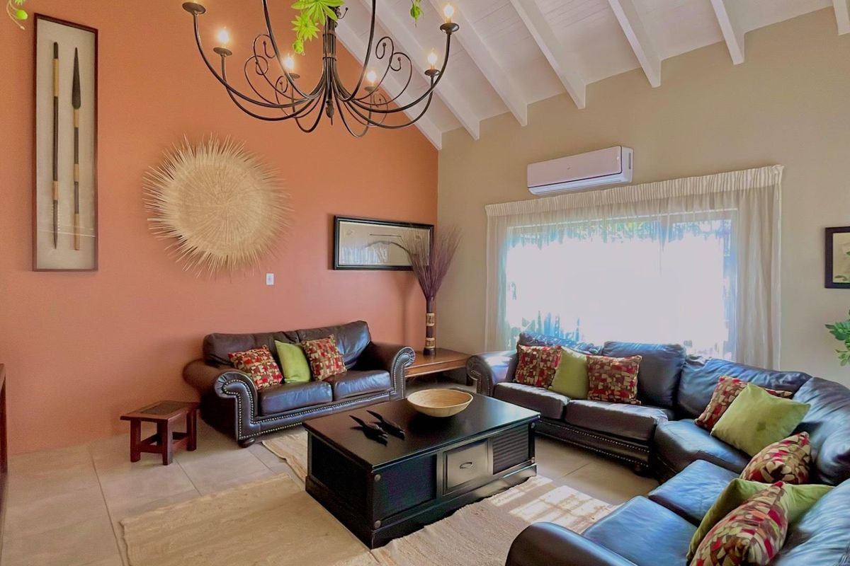 Spacious living room featuring high vaulted ceilings with exposed beams, tiled flooring, and a wall-mounted air conditioning unit.