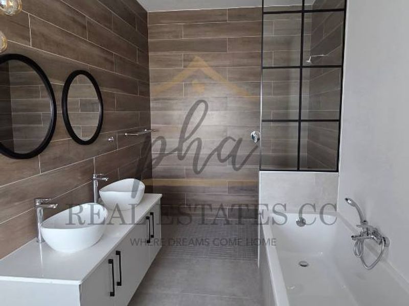 Modern bathroom featuring a double vanity with vessel sinks, a sleek freestanding bathtub, and a stylish glass-panelled shower screen with wood-look tiled feature walls.