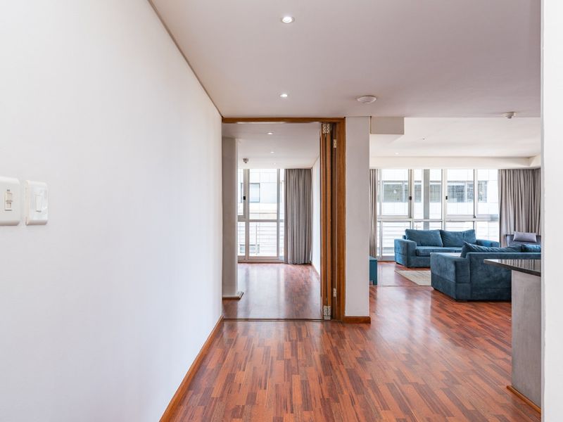 An open-plan living area featuring warm timber flooring, recessed downlights, and large windows that provide ample natural light and access to adjacent spaces.