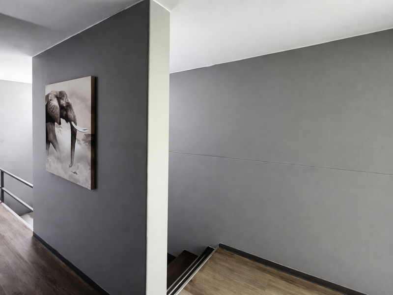 A modern, minimalist hallway featuring grey painted walls, laminate flooring, and a staircase with a metal handrail.