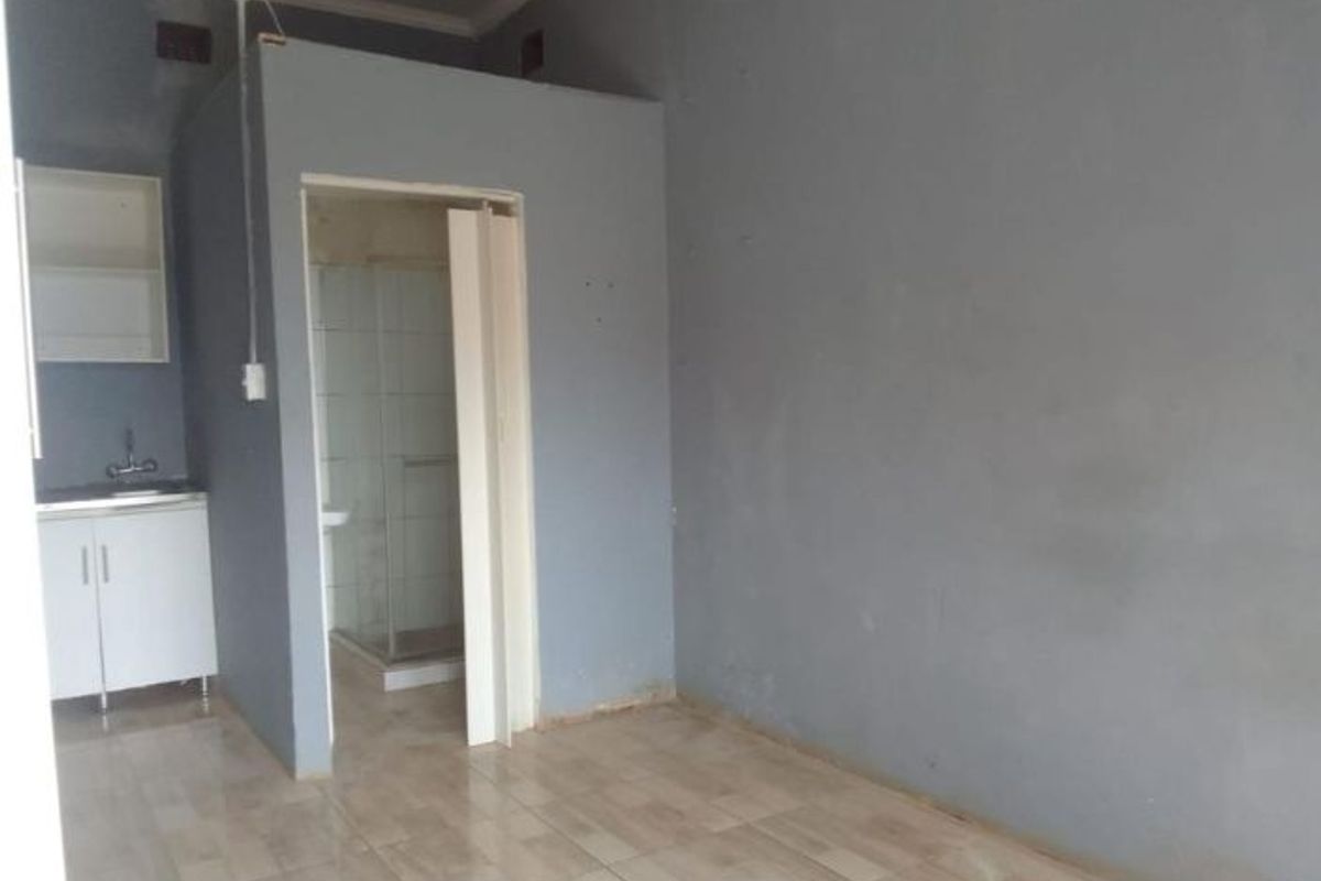 An open-plan living area featuring a compact kitchenette with sink and cabinetry, adjacent to a small enclosed shower room with tiled flooring throughout.