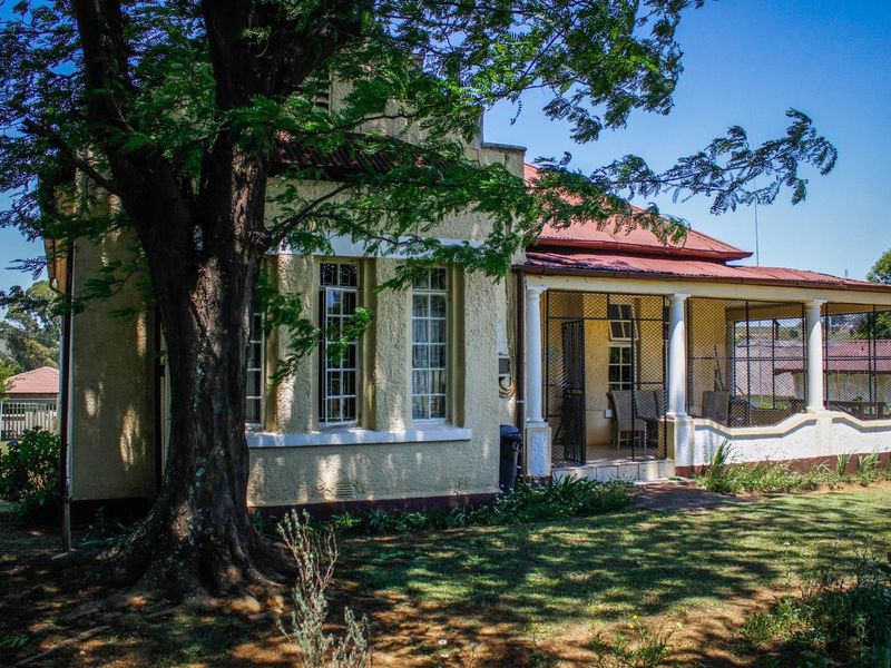 Rear view of the guest house featuring a covered patio area with security gates and traditional multi-pane windows set in a garden.