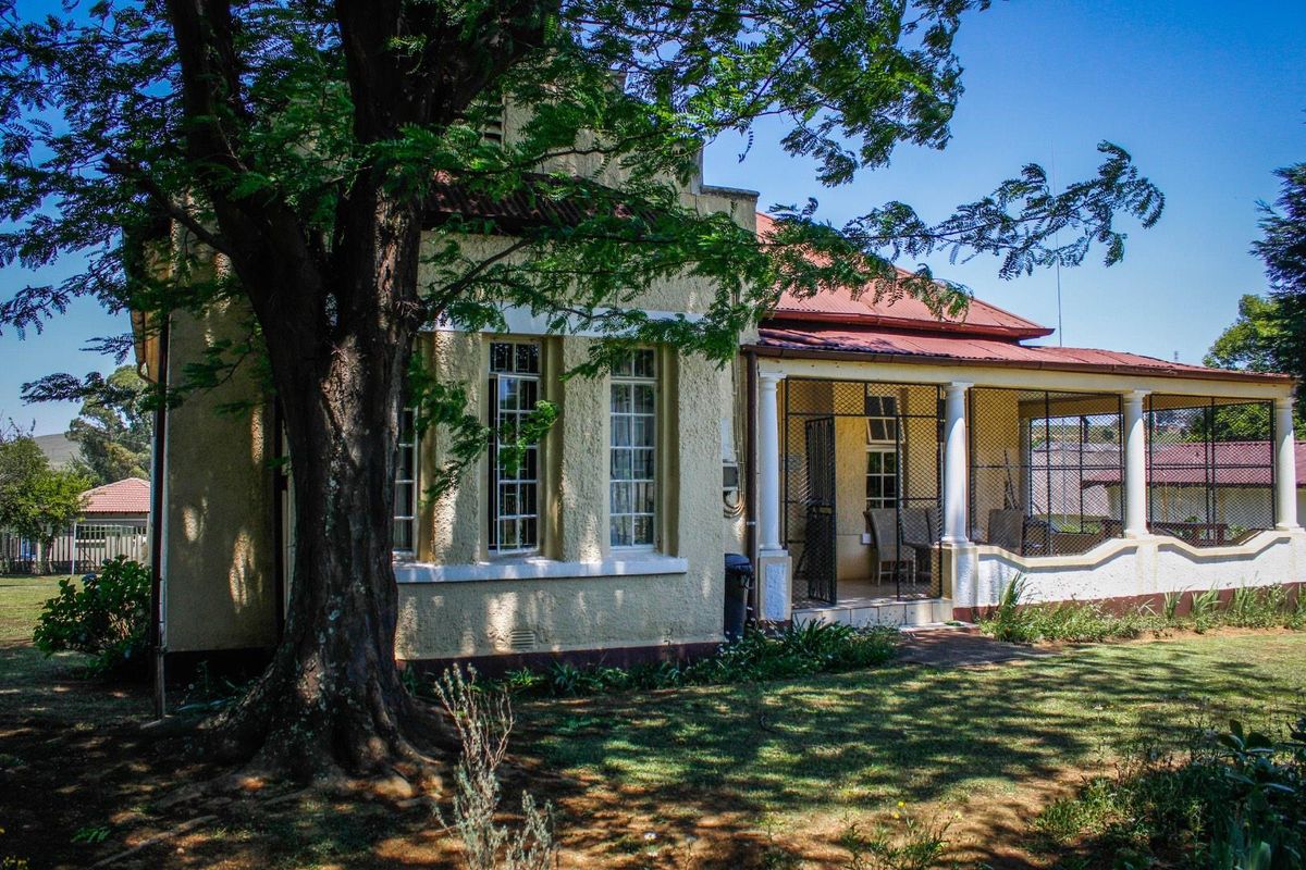 Rear view of the guest house featuring a covered patio area with security gates and traditional multi-pane windows set in a garden.