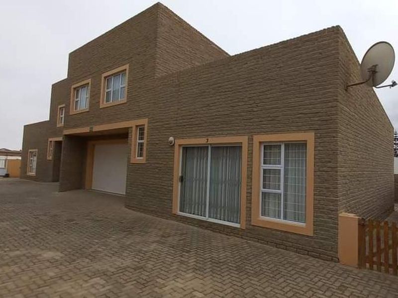 Front elevation of a modern townhouse featuring a textured brick facade, paved driveway, integrated garage, and secure aluminium-framed windows.
