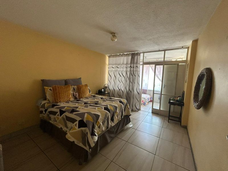 A bedroom featuring tiled flooring and direct access to an enclosed balcony through a glass door.