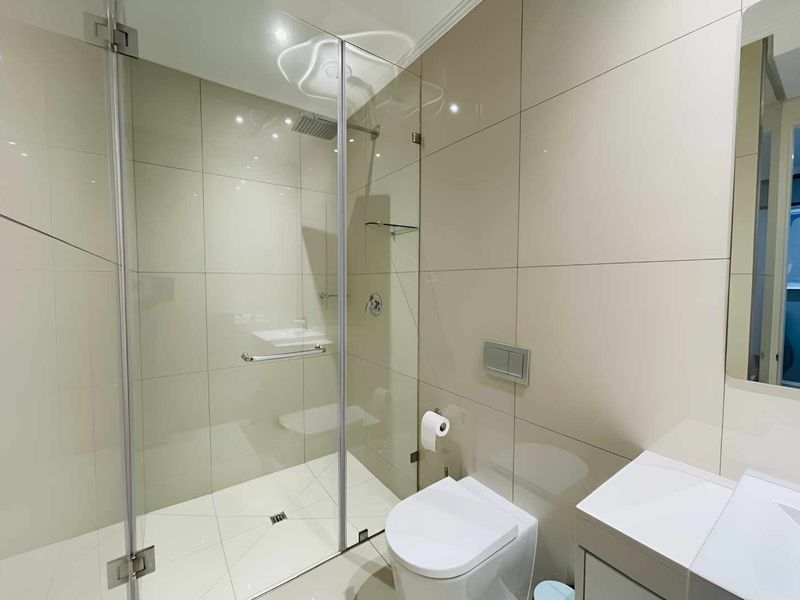 Modern bathroom featuring a glass-enclosed shower with a rain shower head, wall-mounted toilet, and a sleek vanity unit with neutral wall tiling.