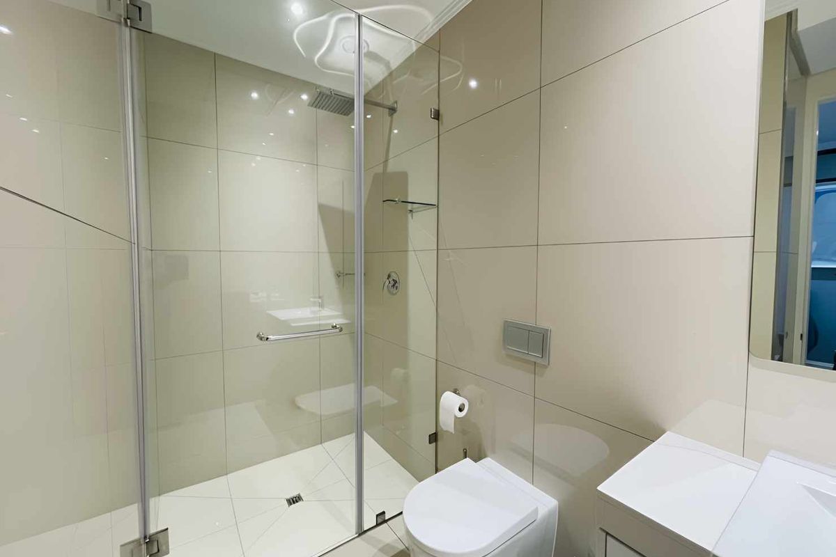 Modern bathroom featuring a glass-enclosed shower with a rain shower head, wall-mounted toilet, and a sleek vanity unit with neutral wall tiling.