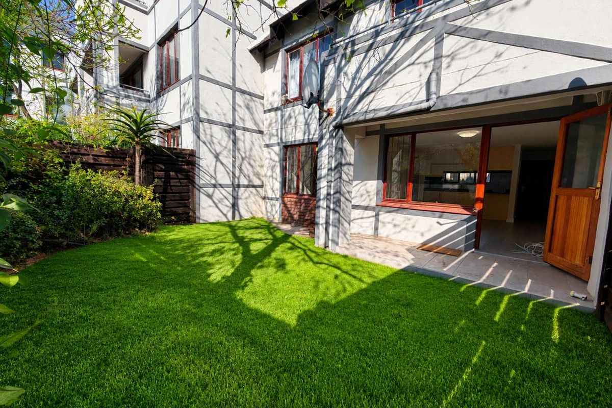 A private rear garden featuring a well-maintained lawn, timber-framed windows, and a paved patio area providing direct access to the apartment interior.
