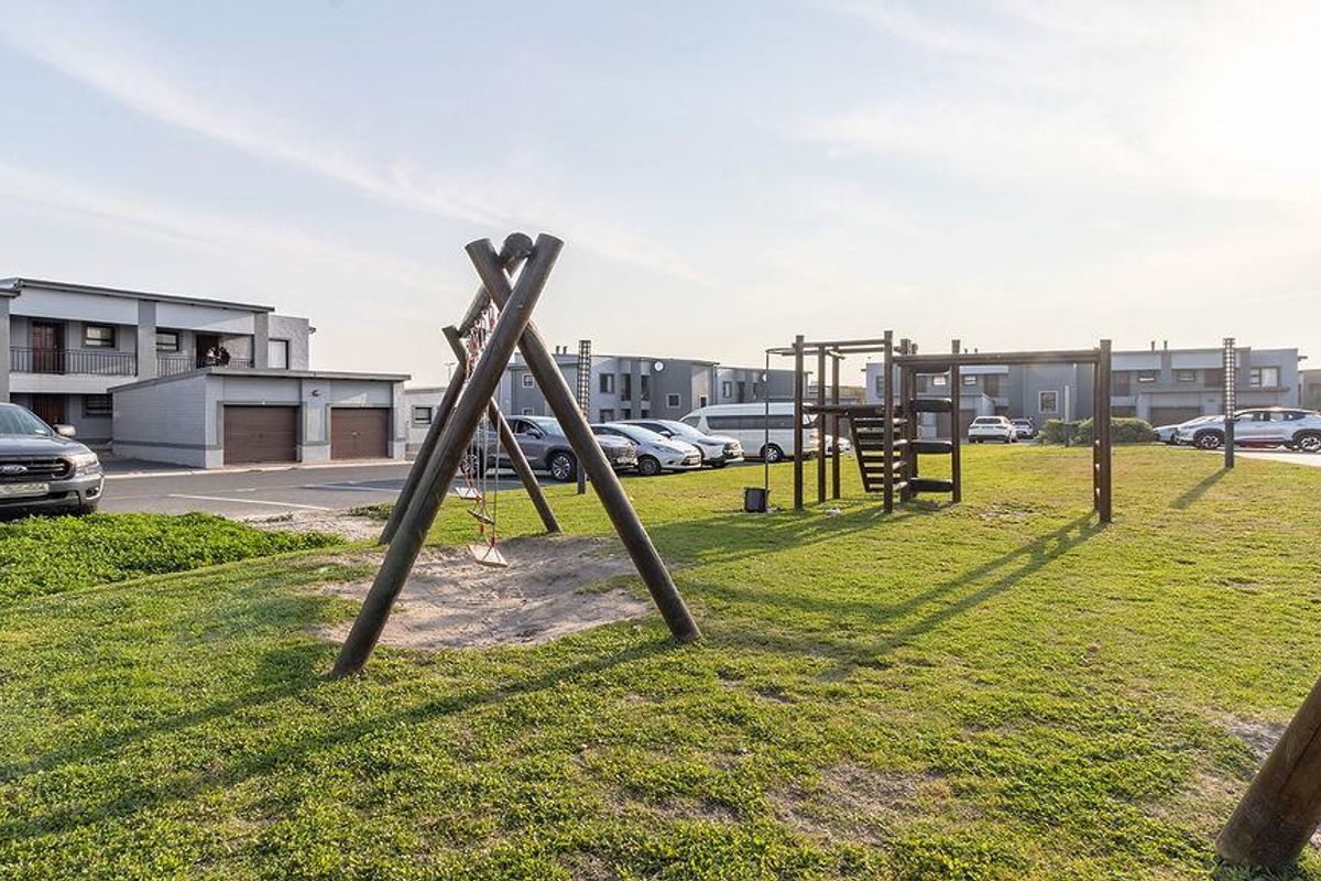 Communal outdoor area featuring a playground, landscaped lawn, and paved parking facilities within the apartment complex.