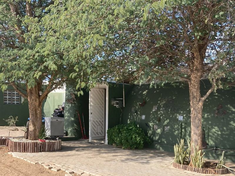 Front exterior view of the property featuring a paved driveway, mature trees, and a secure entrance gate with exterior lighting.