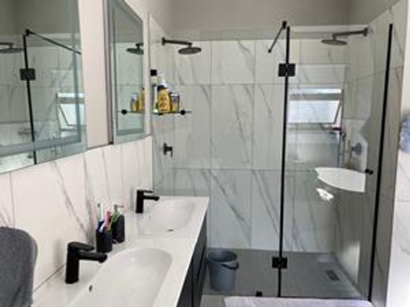 Modern bathroom featuring a double vanity with black tapware, marble-look wall tiles, and a spacious walk-in shower with a glass screen.