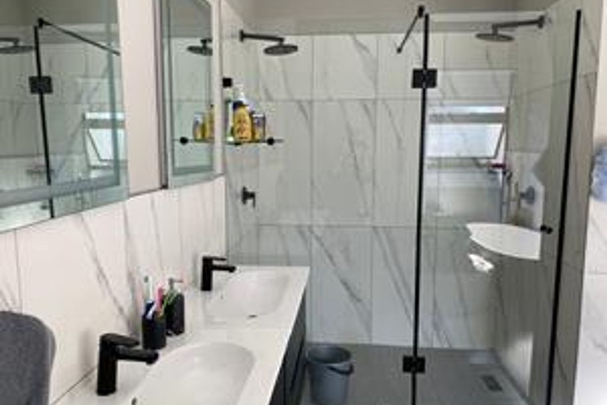 Modern bathroom featuring a double vanity with black tapware, marble-look wall tiles, and a spacious walk-in shower with a glass screen.